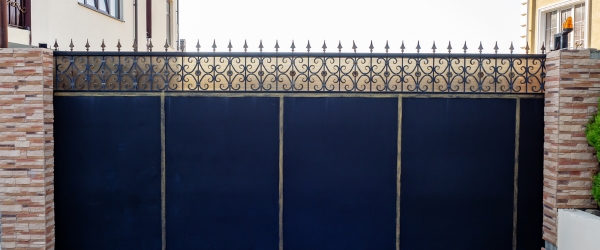 Black iron gate with wrought iron patterned top. Iron black sliding gates with patterned forged edging enclose the private area.